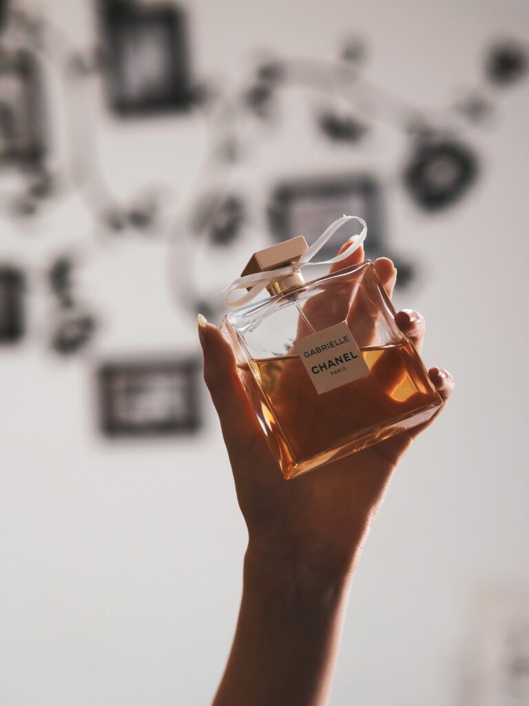 Person gently holding a clear glass perfume bottle, sensitive skin fragrance use